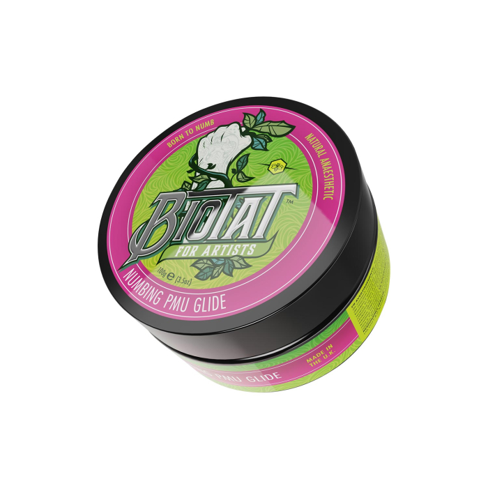 Une boîte ronde de Gel PMU anesthésiant BIOTAT 100 g, destinée aux artistes, avec une étiquette rose et verte vive ornée d’une fleur blanche et mettant en avant ses propriétés anesthésiantes naturelles.